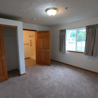 An empty bedroom with carpet flooring, a window with curtains, and an open closet door.