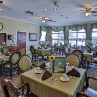A well-arranged dining room with tables set for guests, featuring elegant decor and large windows.