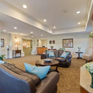 A cozy lounge area furnished with sofas, a coffee table, and decorative elements, featuring carpeted flooring and soft lighting.