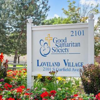 A sign for the Good Samaritan Society's Loveland Village surrounded by flowers and trees.