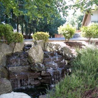A serene garden waterfall surrounded by lush greenery and rocks.