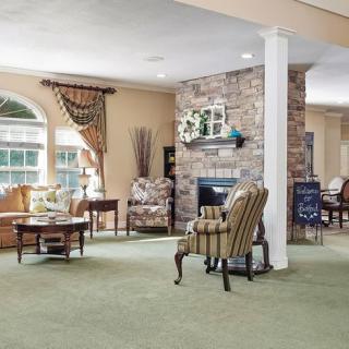 A cozy living room with a fireplace, armchairs, and large windows providing natural light.