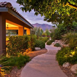 Tranquil garden pathway leading to a house with scenic mountain views at dusk.