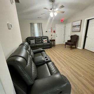 A modern living room featuring leather sofas, a wooden floor, and a ceiling fan.