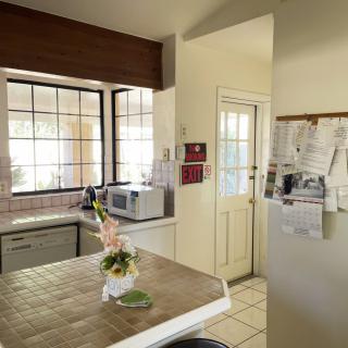 A cozy kitchen featuring a microwave, decorative flowers on the countertop, and large windows letting in natural light.