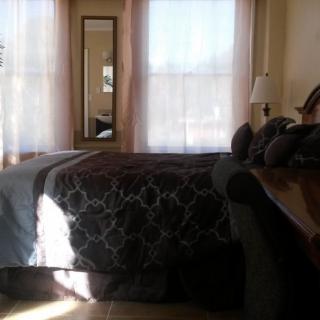 A cozy bedroom with a large bed and sunlight streaming through the windows.