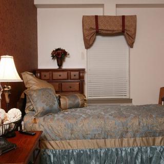 A cozy bedroom featuring a bed with decorative pillows, a nightstand with a lamp, and a window adorned with drapes.