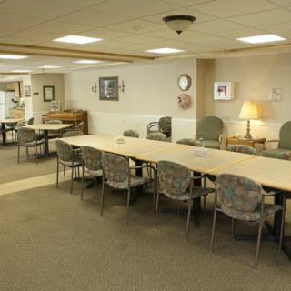 A spacious meeting room with long tables and cushioned chairs, well-lit by ceiling lights.