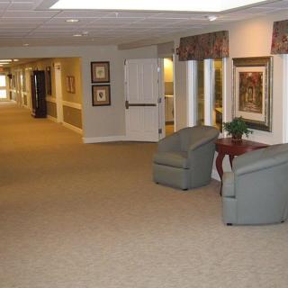 A spacious hallway with comfortable chairs, artwork on the walls, and a potted plant.