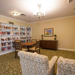 A cozy library room with bookshelves, comfortable chairs, and a table for reading.