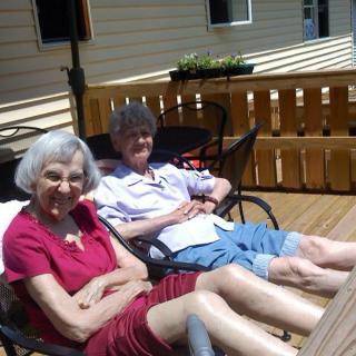 Two elderly individuals sitting and relaxing on a sunny deck.