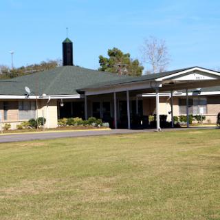 A modern single-story building surrounded by a well-maintained lawn under a clear blue sky.