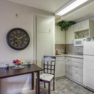 A cozy kitchen with a dining area, featuring a table and chairs, wall clock, and modern appliances.