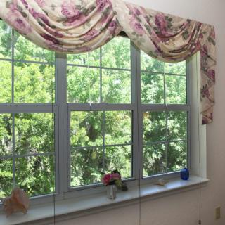 A window with floral-patterned valance, allowing natural light to brighten the interior and revealing a view of lush, green trees outside.