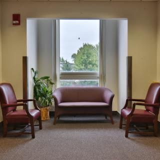 A cozy waiting area featuring a sofa, two chairs, and a plant by the window.