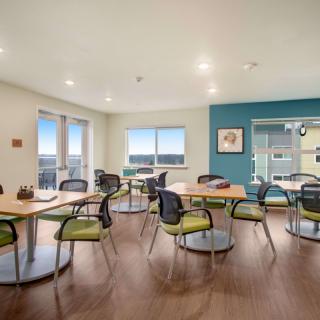 A modern dining area with multiple tables and chairs, illuminated by natural light through large windows.