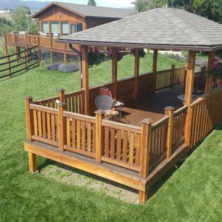 A wooden gazebo located in a backyard, featuring a table and surrounded by green grass.