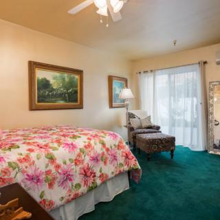 A cozy bedroom featuring a floral bedspread, green carpet, and natural lighting.