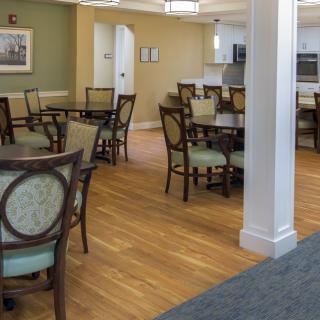 An empty dining room with multiple tables and chairs arranged on a wooden floor.