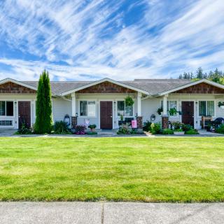 A suburban triplex with well-maintained lawns under a clear blue sky.