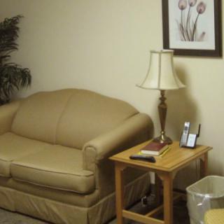 A cozy living room corner with a beige sofa, wooden side table, lamp, and wall art.