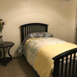 A cozy bedroom featuring a bed with floral bedding, a yellow blanket, and a nightstand with flowers.