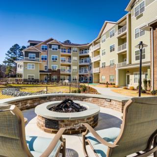 An inviting outdoor space with a fire pit and seating area in front of a modern apartment building.