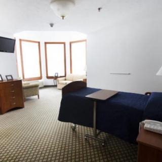 A spacious hospital room with a patient bed, television, and seating area by large windows.