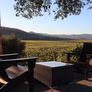 A tranquil outdoor seating area overlooking a vineyard with mountains in the background during sunset.