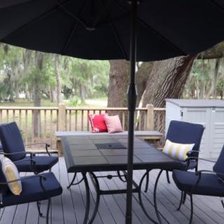A cozy patio setup with chairs and a table under an umbrella on a wooden deck surrounded by nature.