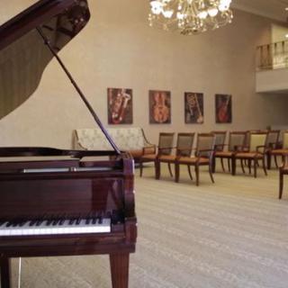 A spacious room featuring a grand piano and a row of chairs with artwork on the wall.