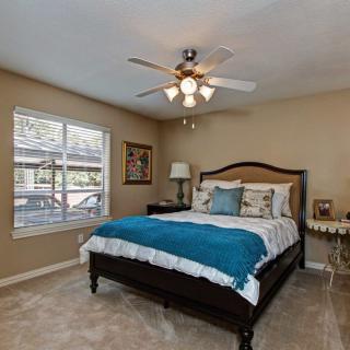 A cozy bedroom featuring a neatly made bed with a blue throw, flanked by bedside tables and illuminated by a ceiling fan light.
