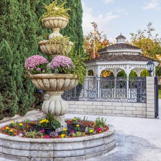 A beautiful garden scene featuring a tiered fountain adorned with pink flowers and a charming gazebo in the background.