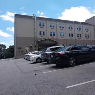 A view of a parking lot in front of a building, with several cars parked and a partly cloudy sky.