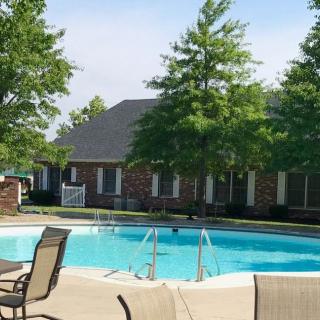 A tranquil outdoor pool area with surrounding trees and a house in the background.
