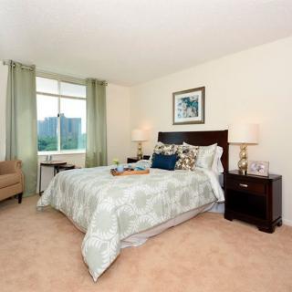 A well-decorated bedroom featuring a bed, nightstands with lamps, and a window allowing natural light.