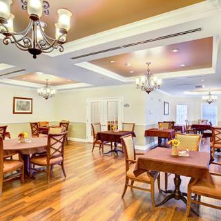 A spacious and elegantly designed dining area with multiple tables and chairs, featuring chandeliers and wooden flooring.