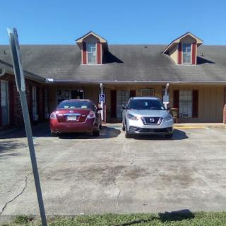 A suburban house with two parked cars in the driveway under a clear blue sky.