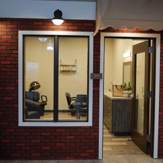 A cozy barbershop with chairs visible through the window, featuring a brick exterior and warm interior lighting.