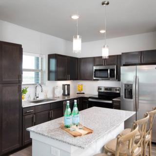 A modern kitchen featuring dark cabinets, stainless steel appliances, and a central island with pendant lighting.
