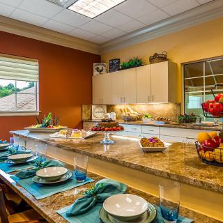 A beautifully arranged kitchen with a granite countertop and dining area set for a meal, featuring fruit displays and elegant place settings.