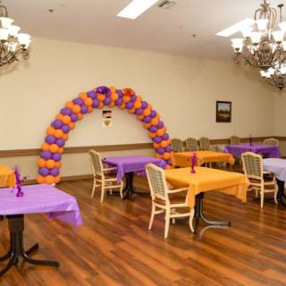 A decorated room with orange and purple balloons forming an arch, and tables covered with matching tablecloths.