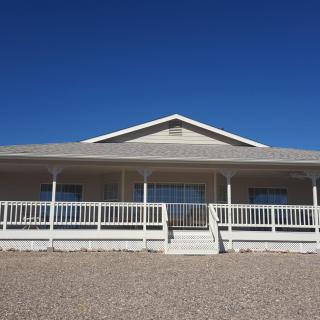A single-story house with a large front porch under a clear blue sky.