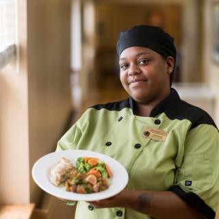 A chef presenting a plated dish in a professional kitchen.