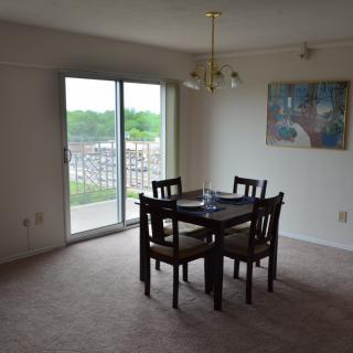 A dining area with a table and four chairs, featuring a sliding glass door leading to a balcony and wall art for decoration.
