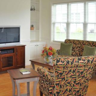 A cozy living room with patterned armchairs, a wooden entertainment center, and large windows.