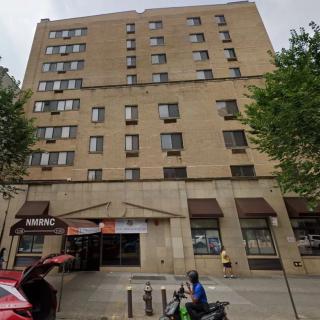 An urban apartment building with storefronts and people on the sidewalk.