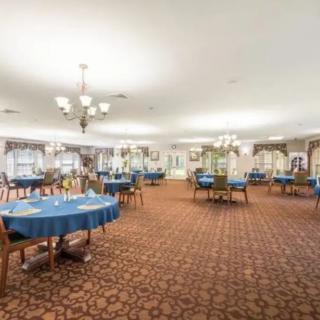 A spacious dining room with tables set for service, featuring blue tablecloths and elegant chandeliers.