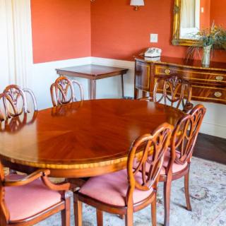 A traditionally styled dining room with a wooden oval table and matching chairs, set against warm-colored walls.