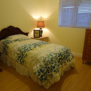 A cozy bedroom with a single bed, nightstand, and a lamp in soft lighting.